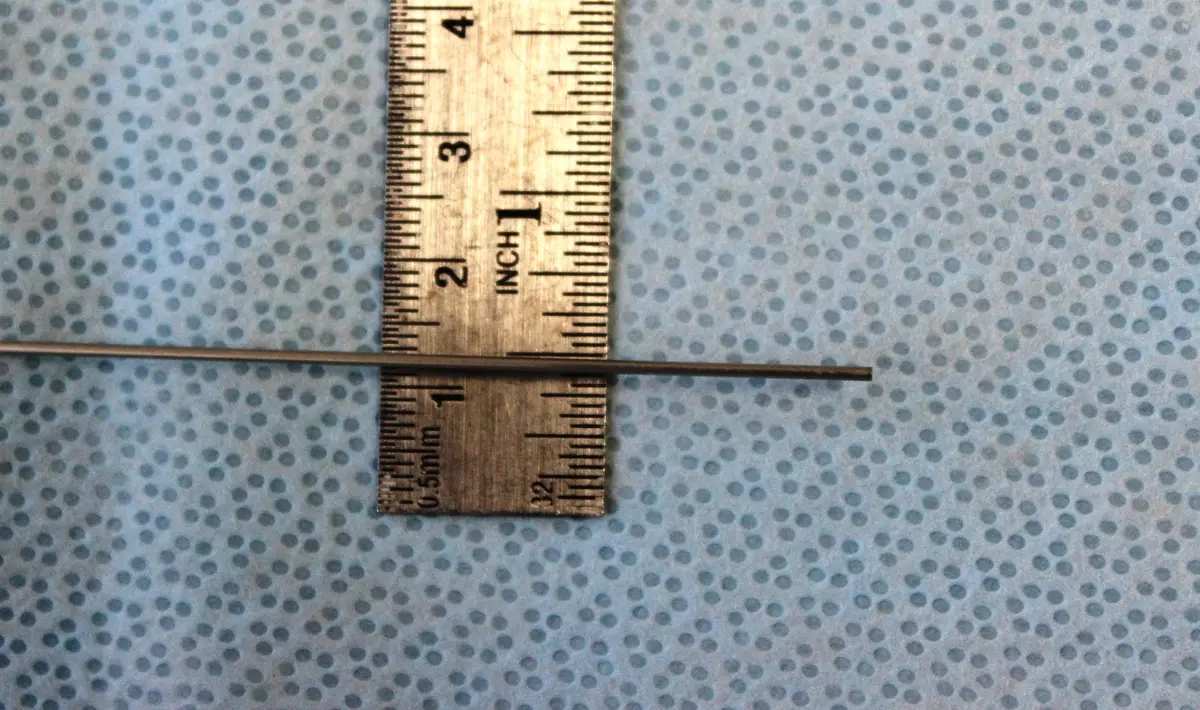 A very thin metal scope laid across a ruler, showing it is about a millimetre wide.