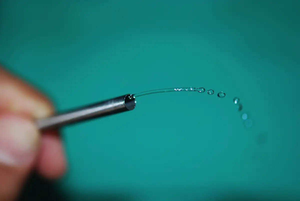 A thin sheath held between fingers with a jet of saline coming from its tip.