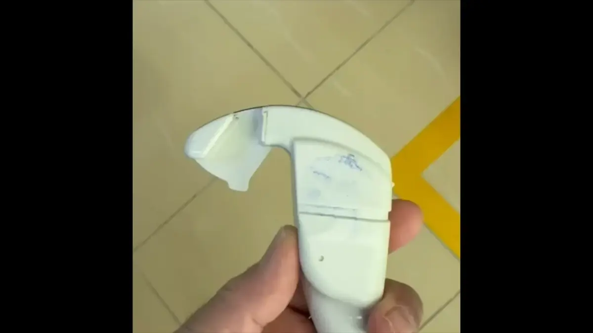A hand holding an ultrasound probe fitted with a needle guide that runs in line with the probe.