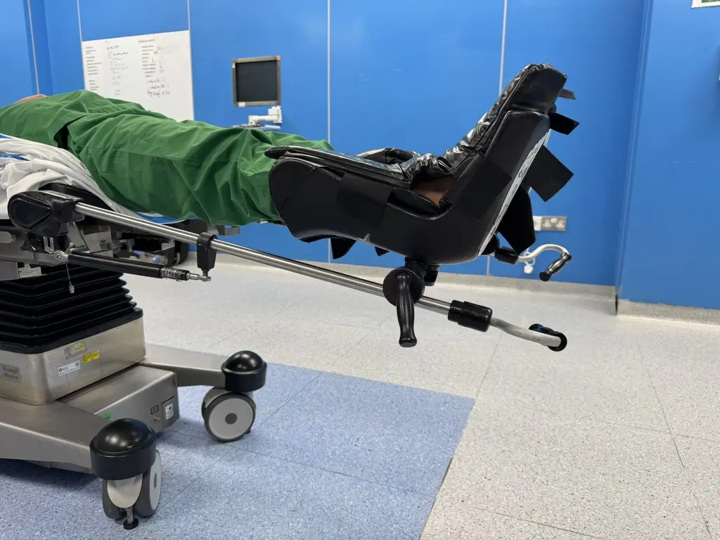 An operating table set up for supine surgery, demonstrated by a person in green scrubs lying flat with legs in supports.